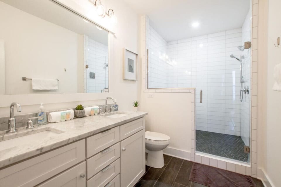 Master bathroom with double vanity, marble countertop, large mirror, and dark tile shower