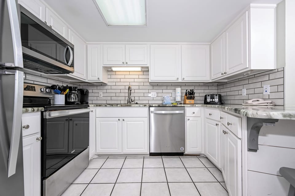 Bright white cabinetry and marbled countertops define this kitchen, featuring stainless appliances and a breakfast bar