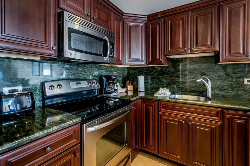 Your fully equipped kitchen features polished granite countertops, rich cherry cabinetry, and modern appliances including a microwave, stove, and coffee maker—perfect for preparing meals at home.