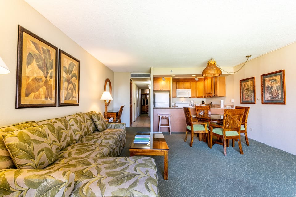 Your open-concept living and dining space flows into a fully equipped kitchen, with tropical artwork, comfortable seating, and warm wood tones creating a welcoming retreat.