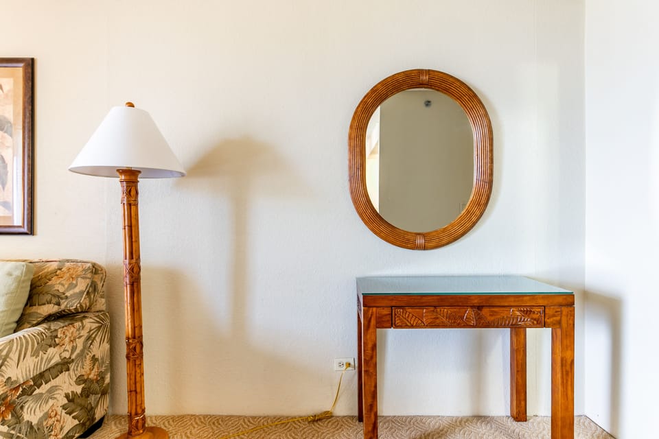 A cozy corner features warm wood furnishings with tropical charm—a woven mirror reflecting light above a carved console perfect for your essentials.