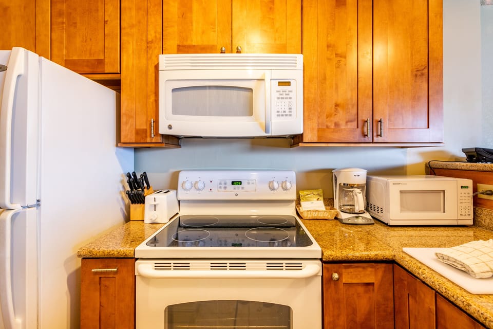 Your fully equipped kitchen awaits with warm wood cabinetry, granite counters, stove, microwave, coffee maker, and toaster—everything you need to cook comfortably during your stay.