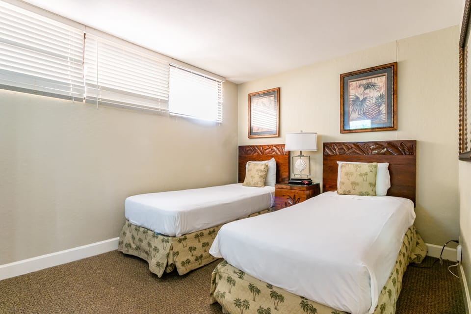 Your cozy guest bedroom features two twin beds with carved wooden headboards, tropical artwork, and soft natural light—perfect for restful nights after island adventures.