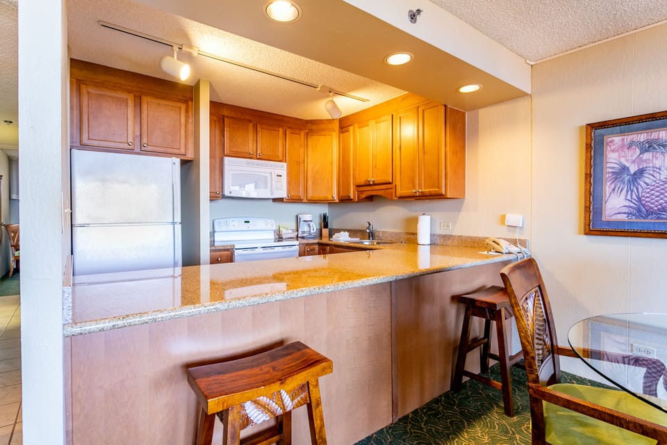 Step into your fully equipped kitchen featuring warm wood cabinetry, granite countertops, modern appliances, and a breakfast bar perfect for morning coffee or quick meals.