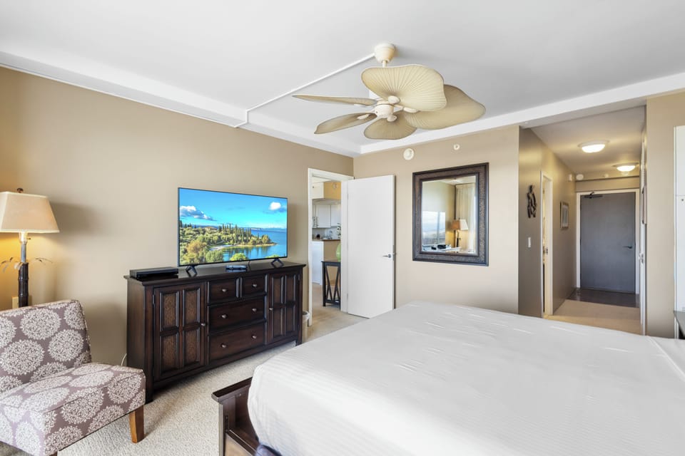 Your bedroom offers a peaceful retreat with a plush bed, tropical ceiling fan, flat-screen TV, and warm coastal décor for ultimate relaxation.