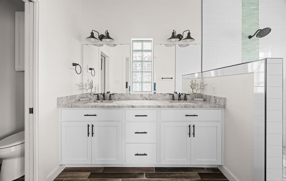 Master Bath — Dual White Vanity, Marble Counter, Black Fixtures, Farmhouse Sconces & Walk-In Shower