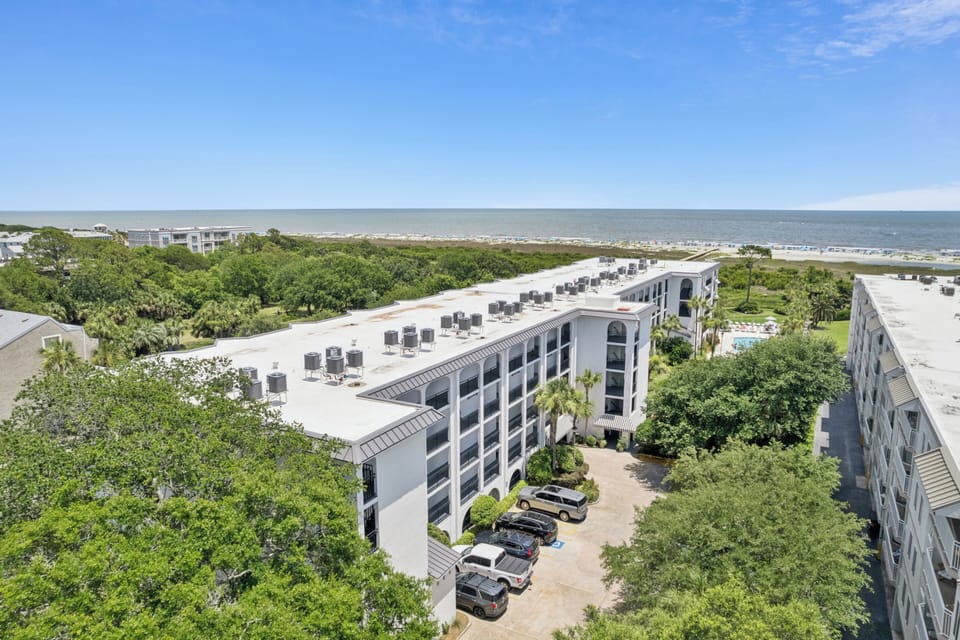 Coastal vacation property nestled between lush greenery and beachfront, featuring rooftop seating areas and nearby beach access in a serene setting.