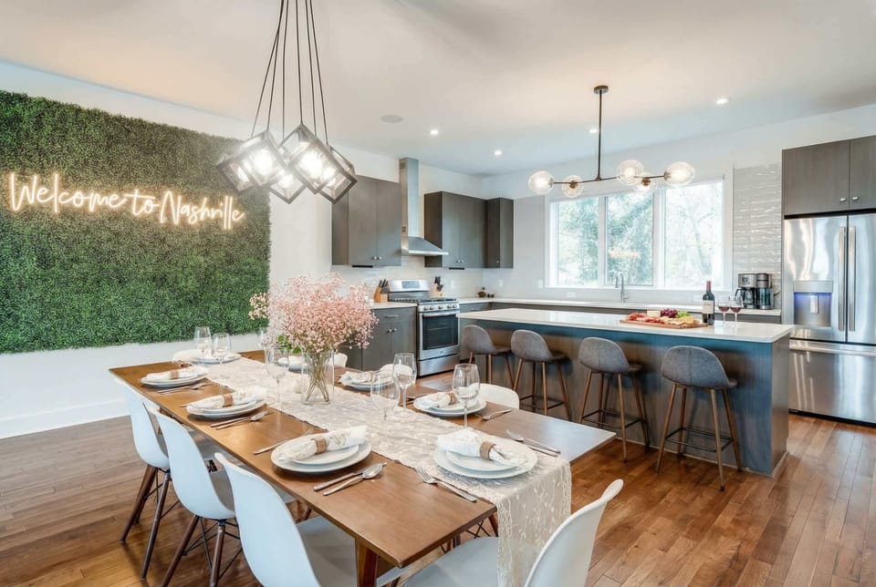 Open kitchen and dining area flow together under contemporary lighting, with the neon sign framed by the artificial plant wall as your backdrop
