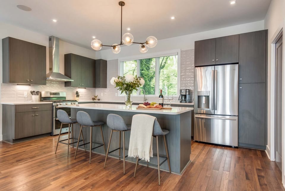 Spacious kitchen with a large island and bar stools makes meal prep a team effort, with pendant lighting and a green view through the window setting the mood