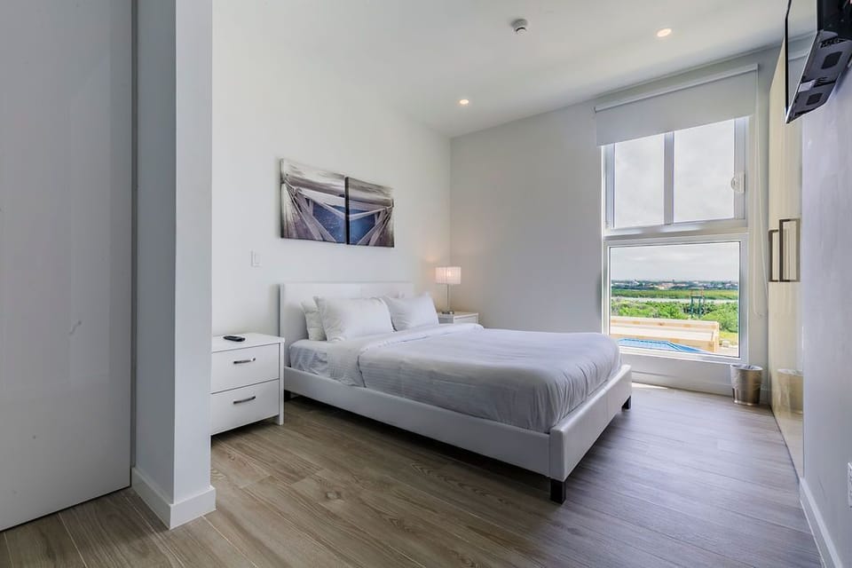 Your peaceful bedroom retreat features crisp linens and a large window framing views of lush greenery and the sparkling pool below.