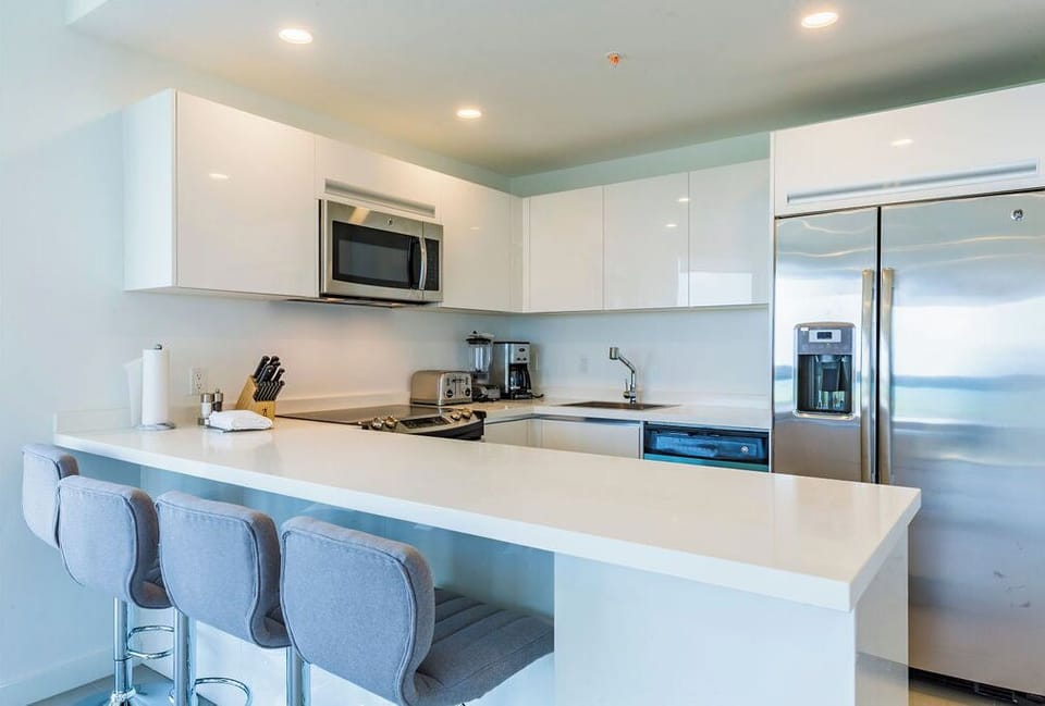 Your bright, modern kitchen features sleek white cabinetry, stainless steel appliances, and a spacious breakfast bar—perfect for morning coffee or preparing meals while enjoying ocean views.