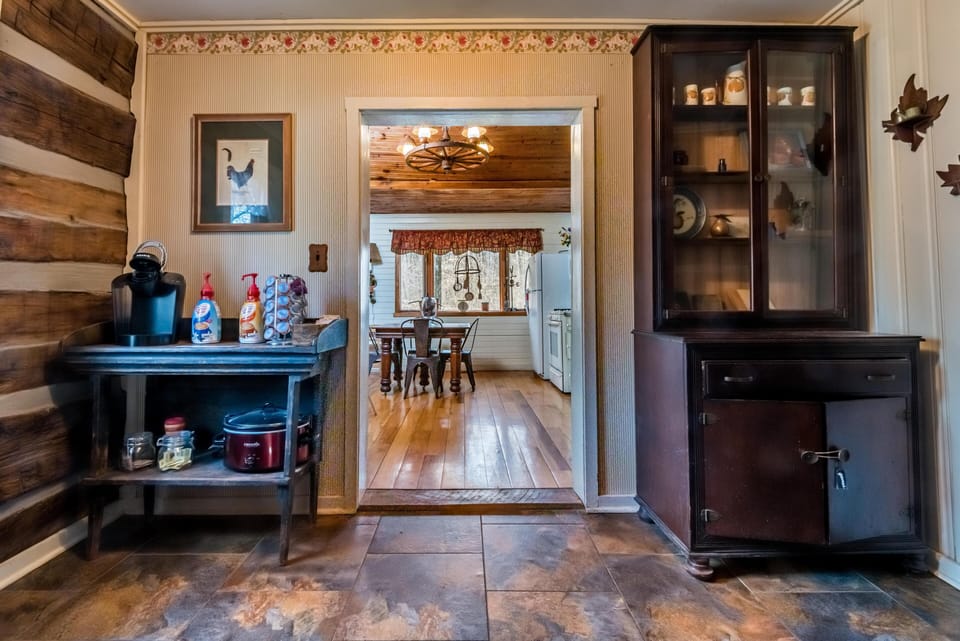 Entryway with stone tile flooring opens to a dining room featuring wood floors, metal chairs, and wagon wheel chandelier.
