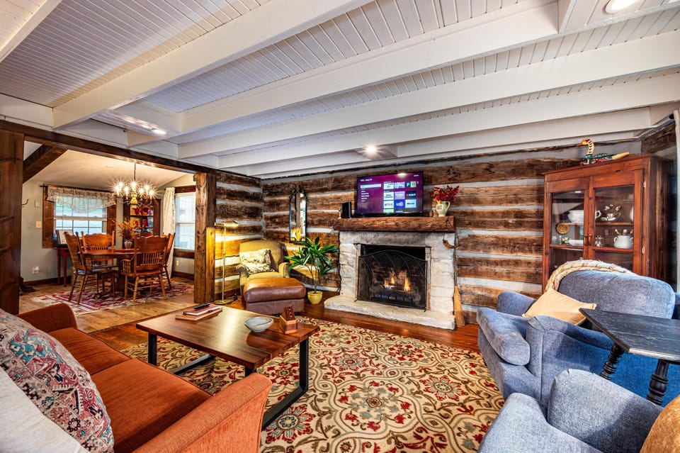 Bedroom with wood-paneled ceiling, carved wood headboard, patterned area rug, and large double windows overlooking trees.