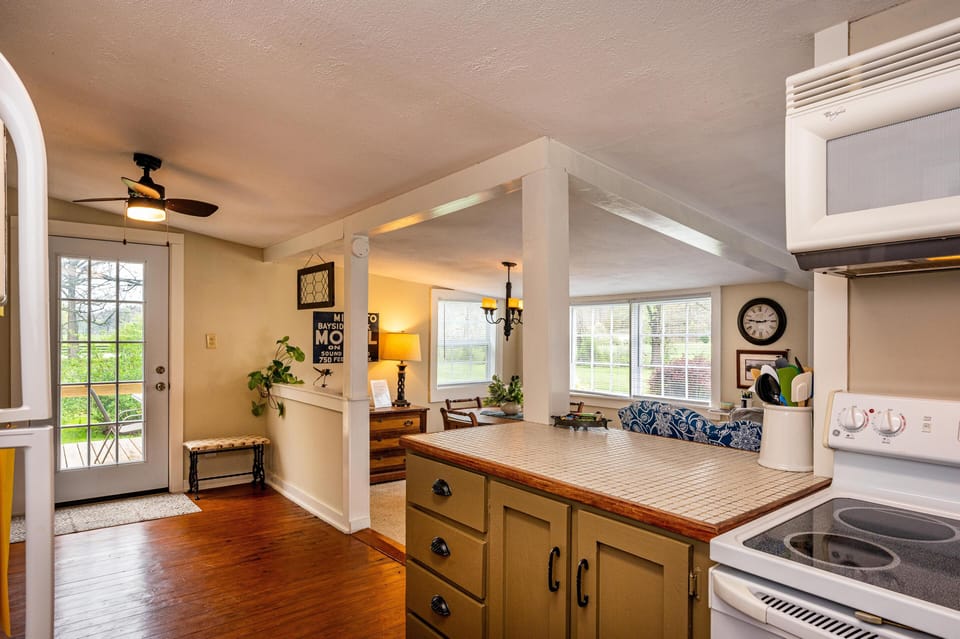Tiled kitchen island with olive green cabinetry overlooks dining area and living room windows.