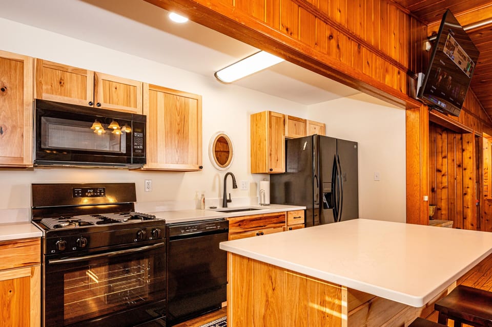Black appliances contrast with natural wood cabinets and white countertops under a ceiling light fixture.