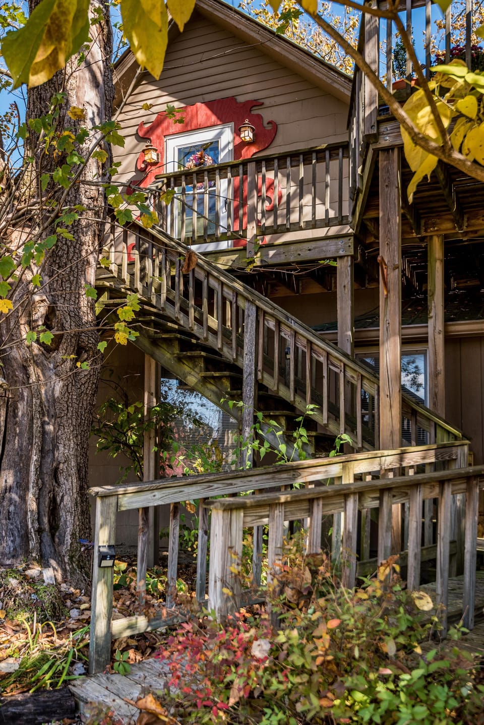 Exterior view of weathered wooden stairs and ramp leading to second-story apartment door framed by red decorative trim.