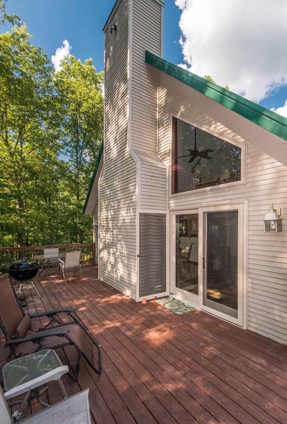 Spacious wooden deck with reclining chairs, charcoal grill, and glass French doors opening to the great room.