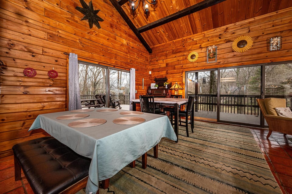 Dining area with wood-paneled walls, vaulted ceiling, patterned rug, and large sliding glass doors to the deck.