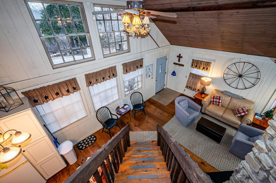 View from loft stairs down to living room with leather couch, blue armchairs, wood floors, and wagon wheel wall decor.
