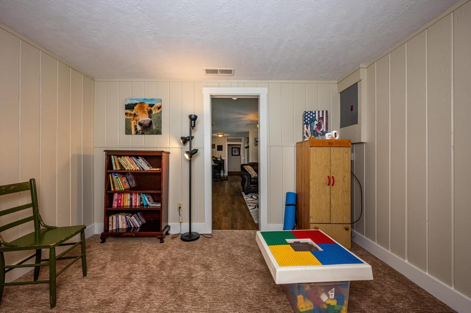 Small playroom with beige panel walls, carpeted floor, wooden bookshelf, and colorful building block table.
