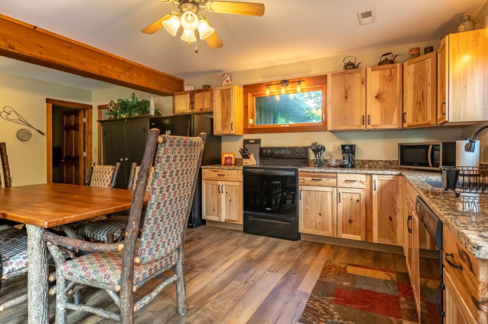 Kitchen features natural wood cabinets, granite countertops, and a black stove beneath a window with warm lighting.
