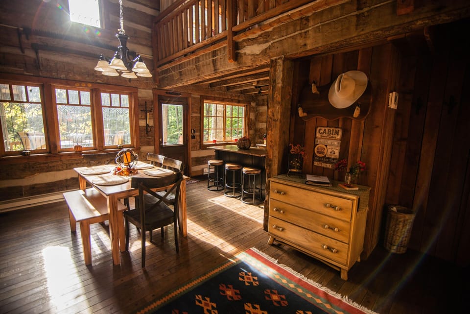 Sunlight filters through leaded glass windows onto the wood dining table, bench, and stools by the kitchen bar.