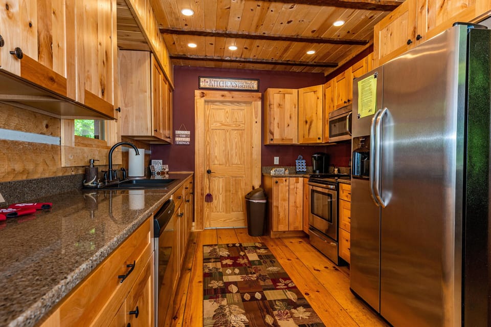 Galley kitchen with alder wood cabinets, granite countertops, stainless steel appliances, and a patterned rug.
