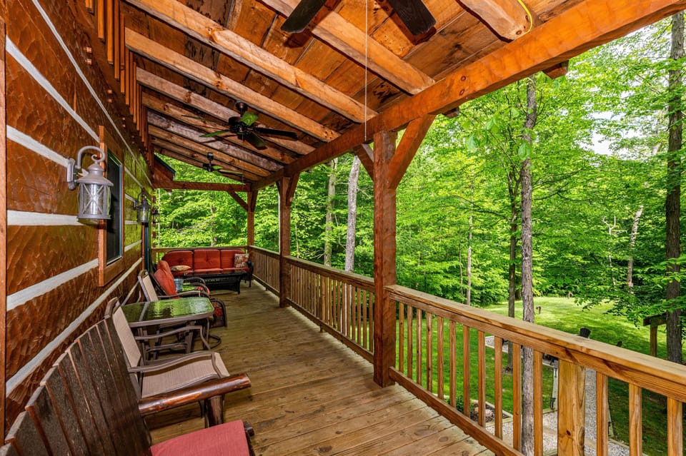 Covered wooden porch with cushioned seating, ceiling fans, lantern-style wall lights, and forest views.