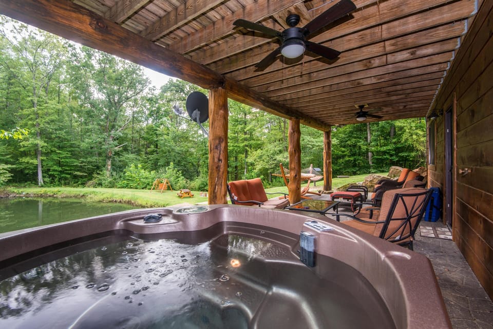 Bubbling hot tub occupies the covered porch, surrounded by cushioned wrought-iron chairs and rustic log beams.