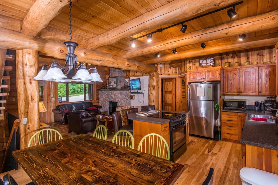 Rustic kitchen and dining area with knotty pine cabinets, stainless steel appliances, and a dark wood table.