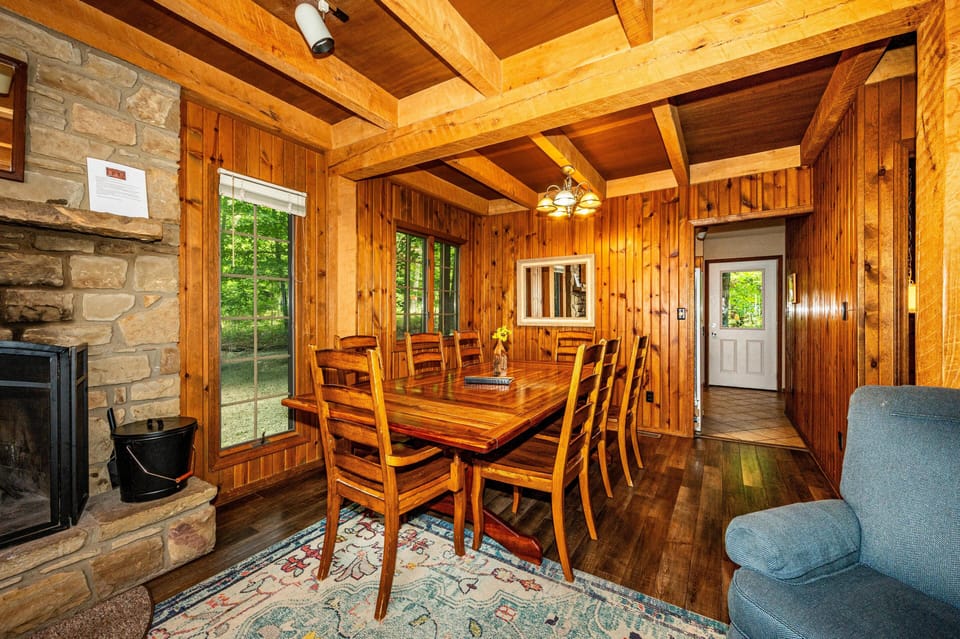 Dining area with polished wood table and eight chairs, paneled walls, stone fireplace, and hardwood floors.