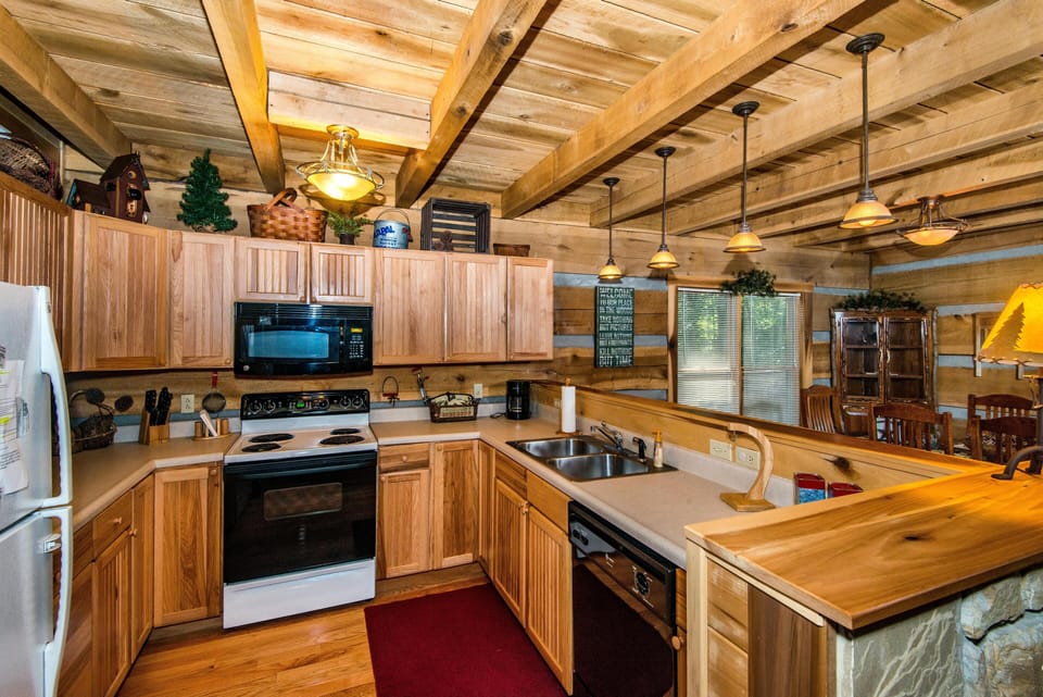 Kitchen with natural wood cabinets, electric stove, double sink, black dishwasher, and pendant lights over breakfast bar.