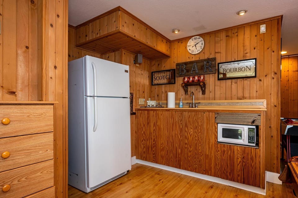 Wood-paneled kitchen area with white refrigerator, built-in microwave, and bar signage above the sink.