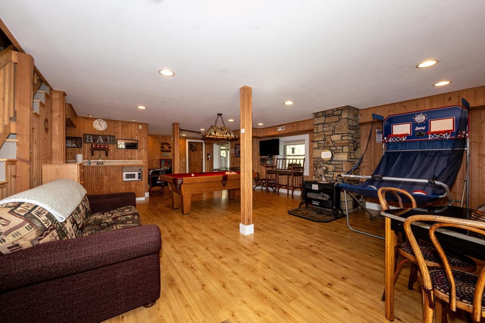 Recreational living room with wood floors, stone fireplace, pool table, arcade basketball game, and mini bar area.