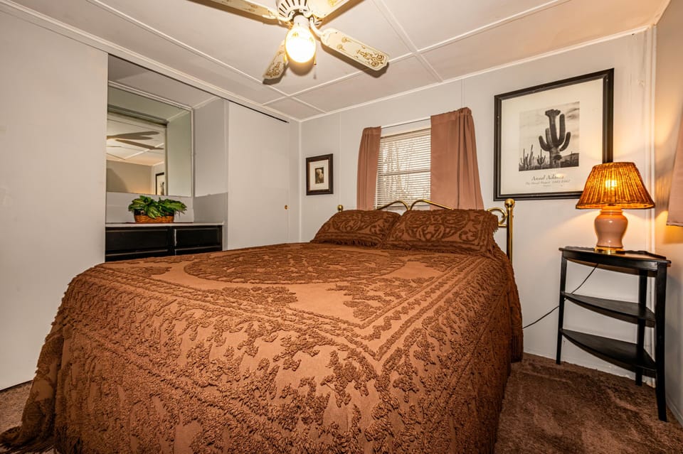 Bedroom with patterned brown bedspread, brass headboard, carpeted floor, wood-framed art, and a lit table lamp.