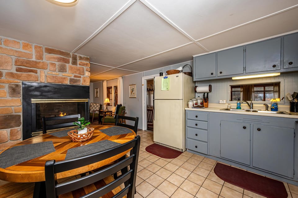 Kitchen and dining area with pale blue cabinets, beige tile floor, wooden table, and stone fireplace.