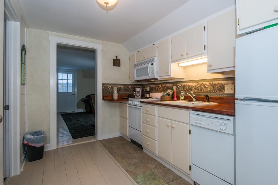 Galley kitchen with cream cabinetry, wood countertops, floral backsplash border, and white appliances.