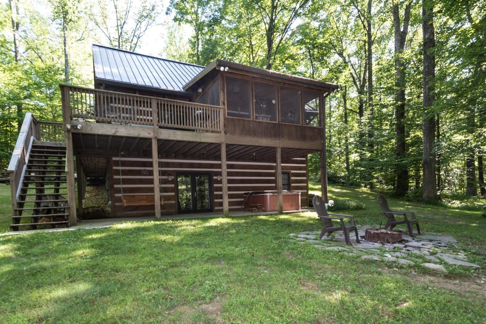 Ground-level fire pit area with Adirondack chairs beside the cabin’s hot tub and wooden swing bench.
