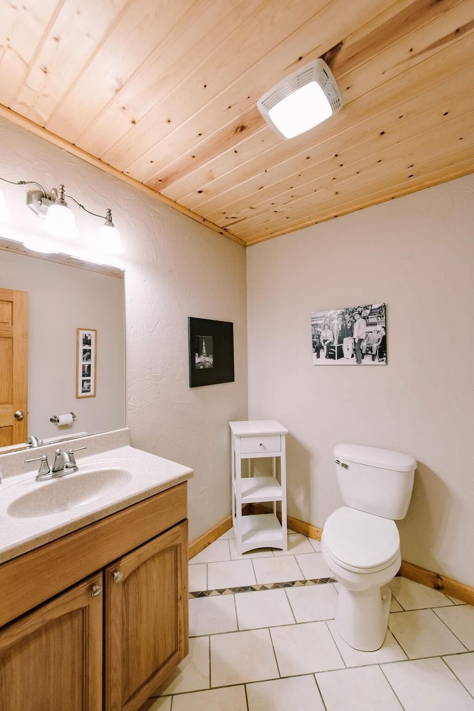 Half bathroom with wood-paneled ceiling, white tile flooring, wooden vanity, and a white storage shelf.