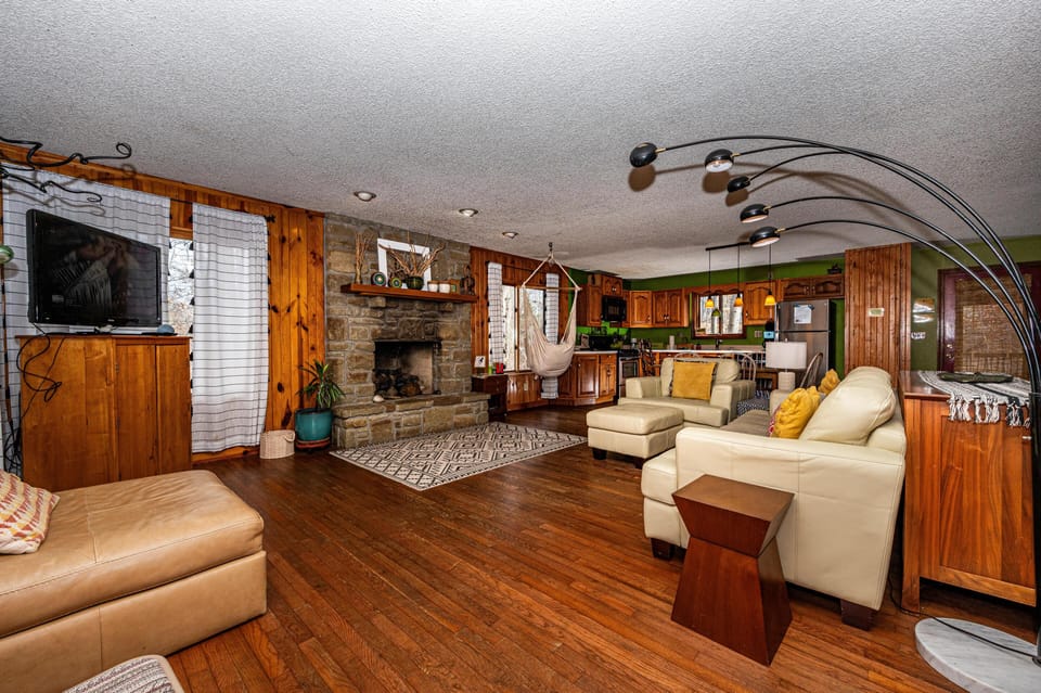 Living room with leather seating, a stone fireplace, wood-paneled walls, and a hanging canvas hammock chair.