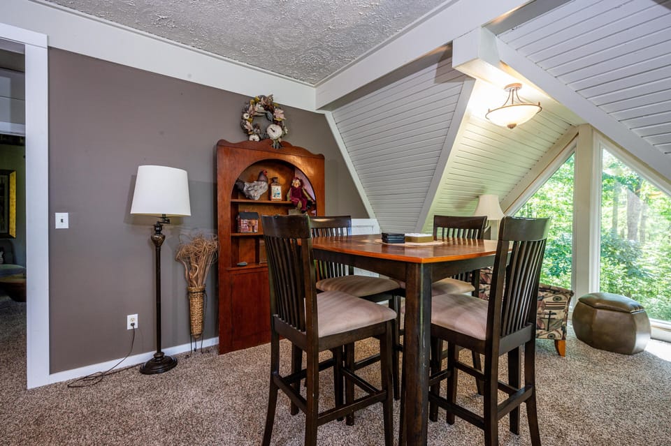Game table with four cushioned chairs sits on plush carpet beneath angled white beadboard ceiling.
