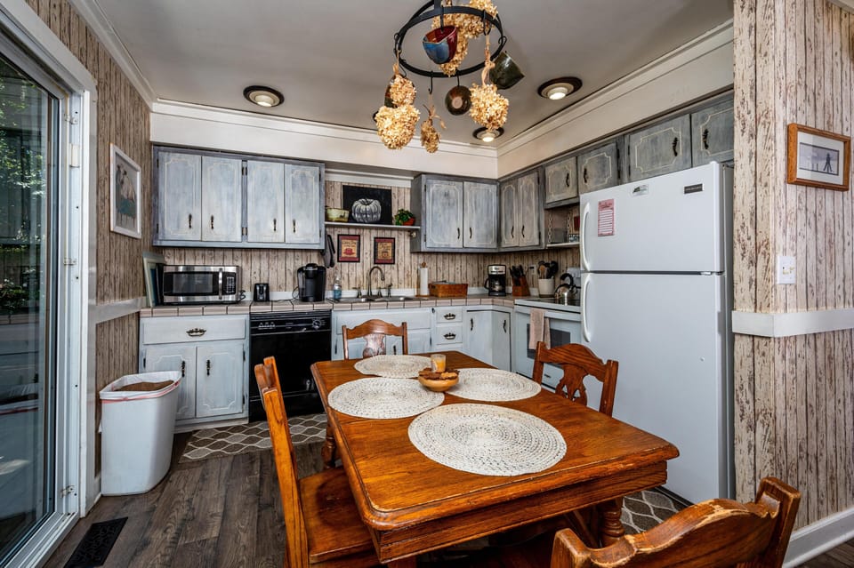 Rustic kitchen with weathered blue cabinets, white appliances, wood dining table, and sliding glass door.