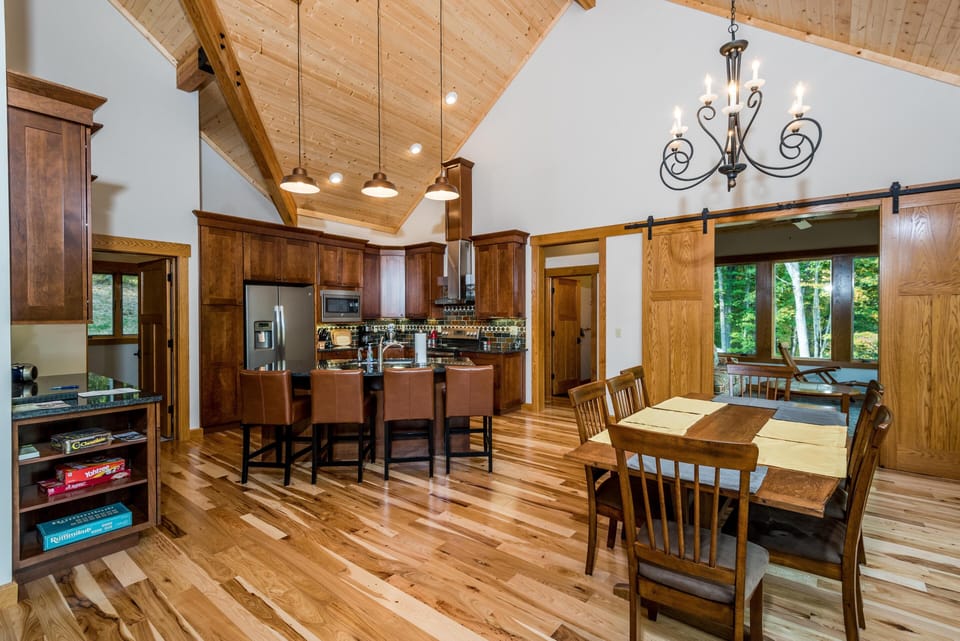 Open-concept kitchen and dining area with polished hardwood floors, wood cabinetry, leather bar stools, and a wrought-iron chandelier.