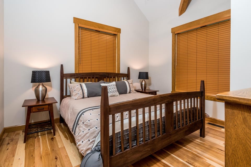 Wood-framed bed with patterned bedding sits between matching nightstands and lamps on natural hardwood floors.