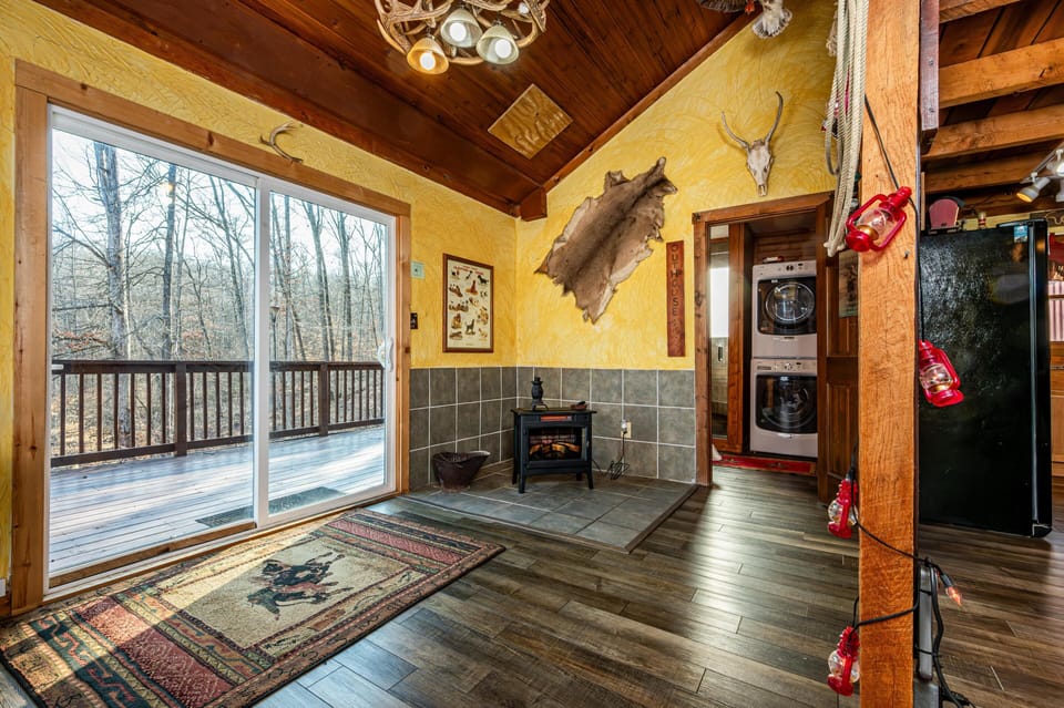 Sliding glass doors open to a wood deck and forest view from the dining area with textured yellow walls and a tile hearth heater.