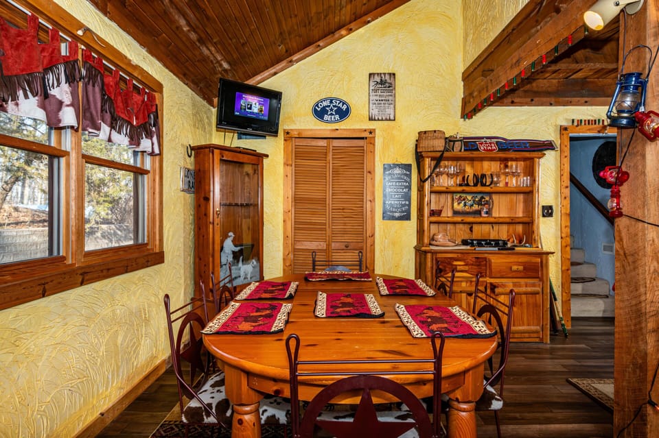 Wood dining table with red animal-print placemats and iron chairs on cowhide cushions under vaulted pine ceiling.