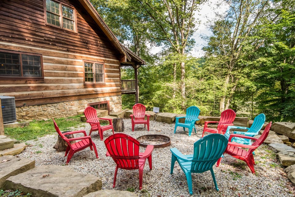 Outdoor fire pit area with red and blue Adirondack chairs arranged on white gravel, surrounded by stone seating walls.