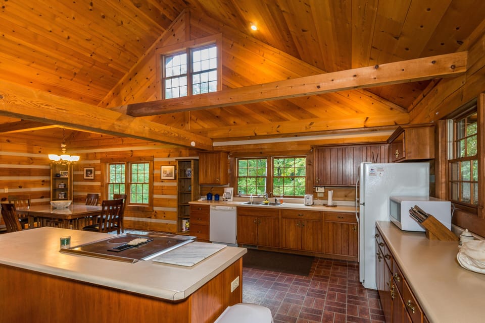 Vaulted ceiling with exposed beams highlights the wood-paneled kitchen featuring a central island and large windows.