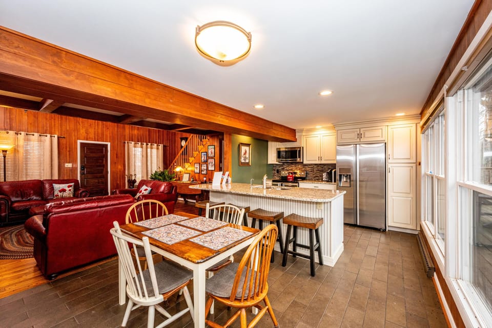 Dining area with mismatched wooden chairs and table placemats adjacent to white kitchen island and stainless steel appliances.