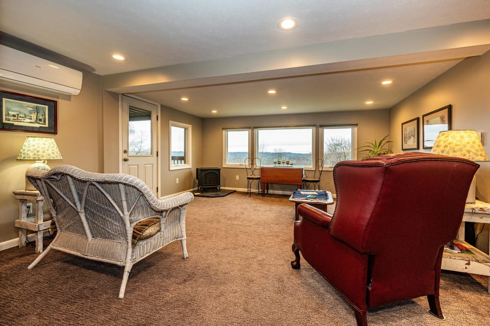 The lower-level living room includes a white wicker loveseat, burgundy leather armchair, and a small wooden table by lamps.